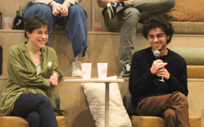 Deux personnes sont attablées avec des verres et l'une pose des questions au micro.