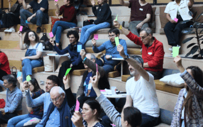 Groupe de gens assis sur des gradins levant une carte de différente couleur chacun pour voter lors de l'agora obsolescence marketing