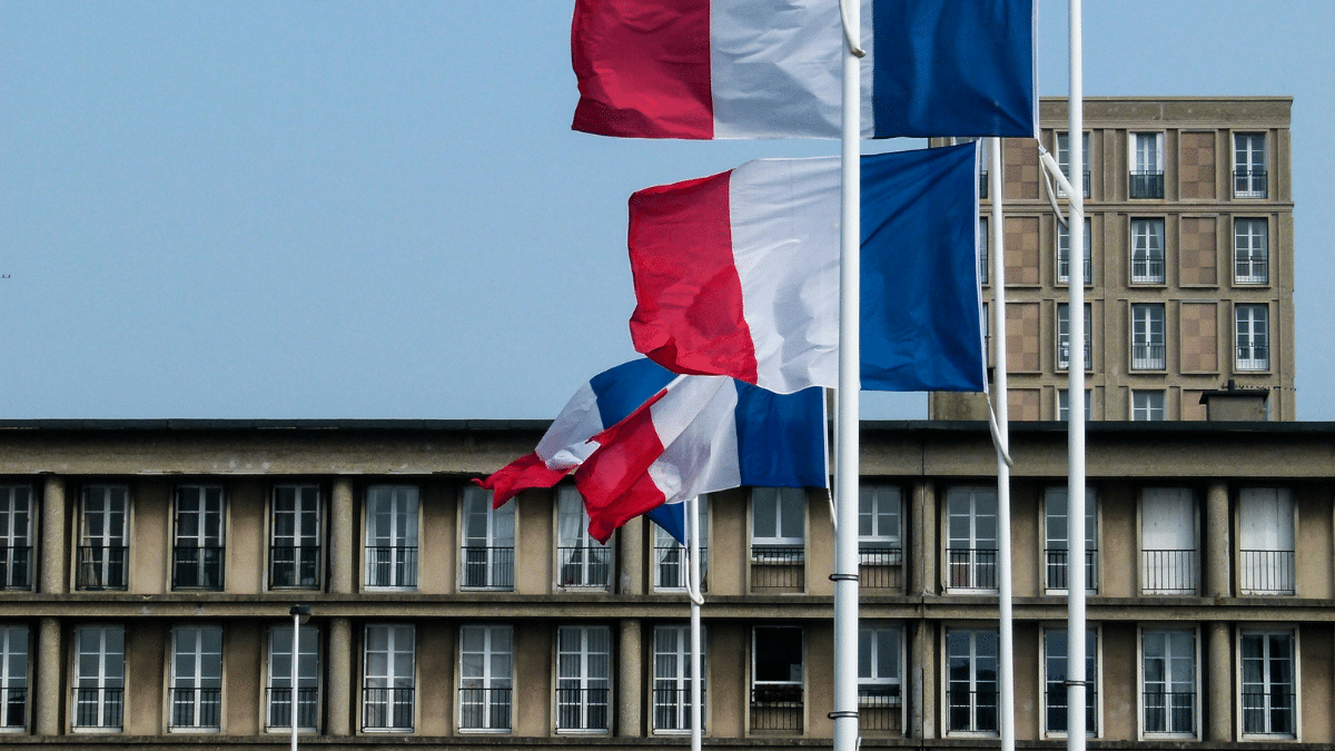 Un bâtiment de collectivités avec des drapeaux français devant qui flottent au vent.