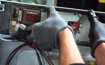 Deux mains avec des gants prisent en gros plan retirent une carte électronique d'un lave-linge.