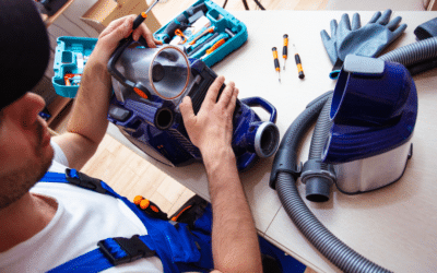 Un réparateur en salopette bleue essaie de réparer un aspirateur démonté.